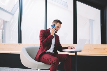 Focused entrepreneur calling on phone using laptop at workplace