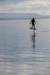 Man riding an electric hydrofoil foil board on a lake with a life jacket