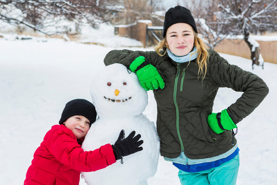 Brother and sister, a young boy and teenage girl leaning on snowman in winter