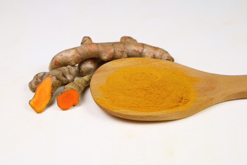 Turmeric powder in a wooden spoon and fresh turmeric roots isolated on a white background is an ingredient in turmeric foods and ingredients in skin care products. Turmeric helps the skin to be strong