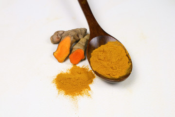 Turmeric powder in a wooden spoon and fresh turmeric roots isolated on a white background is an ingredient in turmeric foods and ingredients in skin care products. Turmeric helps the skin to be strong