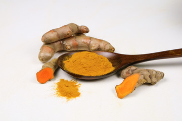 Turmeric powder in a wooden spoon and fresh turmeric roots isolated on a white background is an ingredient in turmeric foods and ingredients in skin care products. Turmeric helps the skin to be strong