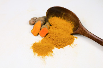Turmeric powder in a wooden spoon and fresh turmeric roots isolated on a white background is an ingredient in turmeric foods and ingredients in skin care products. Turmeric helps the skin to be strong
