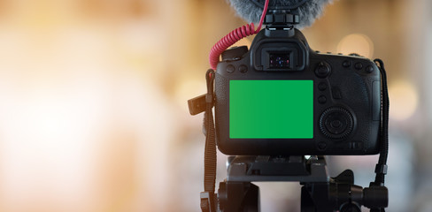 Close Up of the camera on a tripod with a green LCD screen and a recording microphone. Behind and blurred scenes on the background, video, vlog recording or online streaming podcasts. - Powered by Adobe
