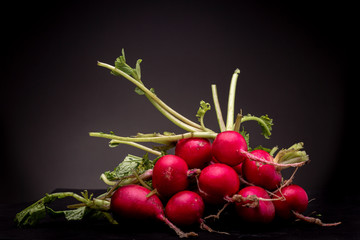 Lot of radishes grouped on a black surface. Still life studio shot of vegetable against a dark background.