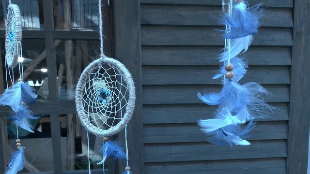 Blue feathers of dreamcatcher hanging in front of the wooden house slowly moving, floating - traditional indian talisman