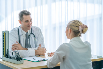 Mature Caucasian male doctor examining and consulting young beautiful woman patient in hospital clinic. Professional general practitioner consultant diagnosis medical healthcare concept