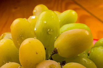large brush of green grapes in a red ceramic plate on a wooden background