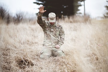 American soldier kneeling in despair on a grass field with his hand raised above