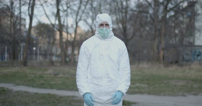 Portrait of male scientist in protective suit showing midle fingers standing in urban daytime park after pandemic coronavirus quarantine time has ended looking in camera 4K