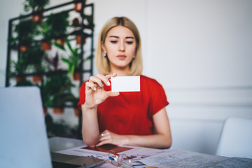 Serious woman holding cutaway in hand and reading information at table in office