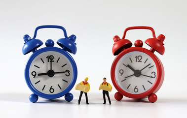 Two miniature couriers standing between a red and blue alarm clock.