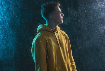 A young guy in a yellow hoodie is sad behind a blind window
