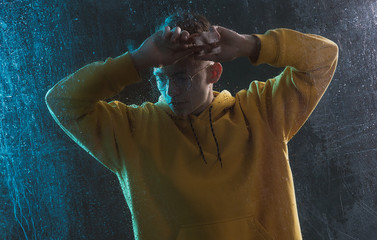 A young guy in a yellow hoodie is sad behind a blind window