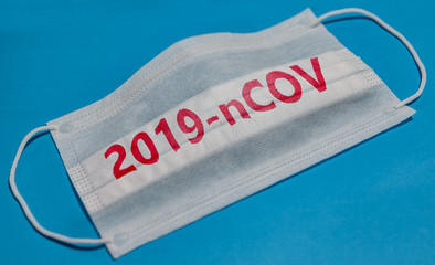 Fototapeta na wymiar Medical face mask with 2019-nCOV text on blue background. Concept of coronavirus quarantine.
