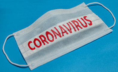 Fototapeta na wymiar Medical face mask with CORONAVIRUS text on blue background. Concept of coronavirus quarantine.