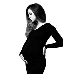 Fototapeta premium Black and white photo of pregnant female in tight dress. She put hands on her belly, posing isolated on white background. Close up