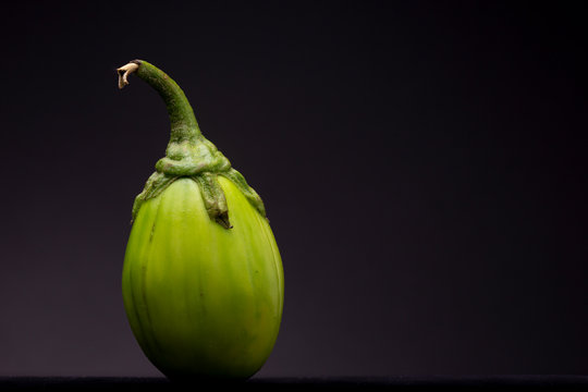 Scarlet eggplant vegetable seen from table height against a dark grey background. Aesthetic still life studio image of food. 