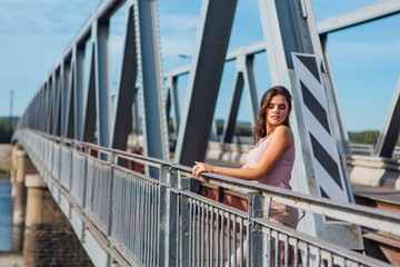 Pretty young woman posing on the old rusty transport bridge over the river during sunset.
