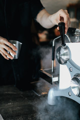 Coffee machine with steam in the process a cafe.Barista Cafe Making Coffee Preparation Service Concept.Barista is pouring coffee in a measure milk glass at the cafe. Close up, selective focus, toned, 