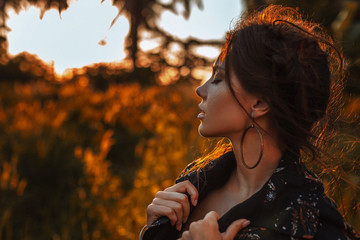 young stylish woman wearing coat posing outdoors at sunset portrait