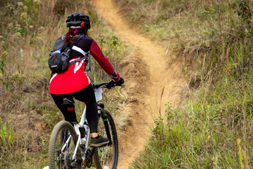 Naklejka premium female cyclist from back with red uniform in mountain biking competition going up