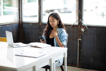 Obraz premium Young businesswoman using mobile phone while sitting with diary and laptop at desk in office