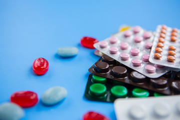 Flat lay composition with bunch of different colorful pills and blister packs in the corner. Pile of unpacked medication on paper textured background. Close up, copy space.