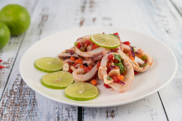 Spicy lemon squid with galangal, chilies, carrots, peppermint, spring onions and garlic on a plate on a white wooden floor.