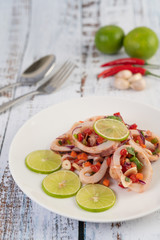 Spicy lemon squid with galangal, chilies, carrots, peppermint, spring onions and garlic on a plate on a white wooden floor.