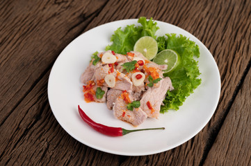 Spicy lime pork with salad, galangal, chilli, tomato and garlic on a white plate on a wooden floor.