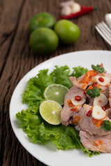Spicy lime pork with salad, galangal, chilli, tomato and garlic on a white plate on a wooden floor.