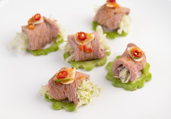 Spicy lime pork salad with bitter melon, galangal, chili, tomatoes and garlic in a white plate on a black cement floor.