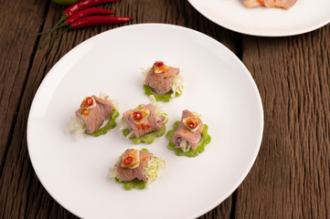 Spicy lime pork salad with bitter melon, galangal, chili, tomatoes and garlic in a white plate on a black cement floor.