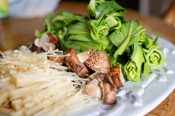plate of raw bok choy enoki and shitake mushrooms for hot pot