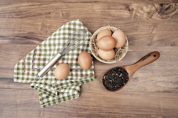 Top view of raw eggs in the basket and Straw or chaff with Egg beater , hand towel and rice berry in the wooden spoon on wooden table.vintage filter.