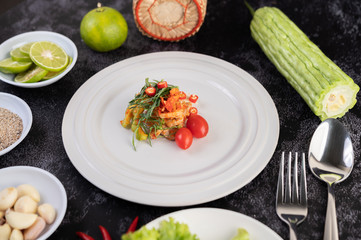 Spicy lime pork salad with bitter melon, galangal, chili, tomatoes and garlic in a white plate on a black cement floor.