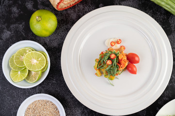 Spicy lime pork salad with bitter melon, galangal, chili, tomatoes and garlic in a white plate on a black cement floor.