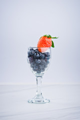 Blueberries and strawberry in a glass of wine on white background.
