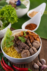 Yellow noodles in a cup with crispy pork, slices of pork, and meatballs together with Thai food-style noodles