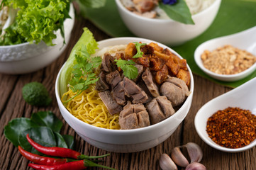 Yellow noodles in a cup with crispy pork, slices of pork, and meatballs together with Thai food-style noodles