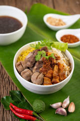 Yellow noodles in a cup with crispy pork, slices of pork, and meatballs together with Thai food-style noodles