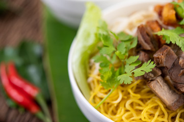 Yellow noodles in a cup with crispy pork, slices of pork, and meatballs together with Thai food-style noodles