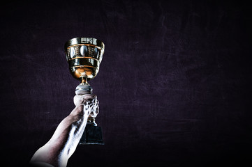 Fototapeta na wymiar Hand holding up a gold trophy cup against dark background