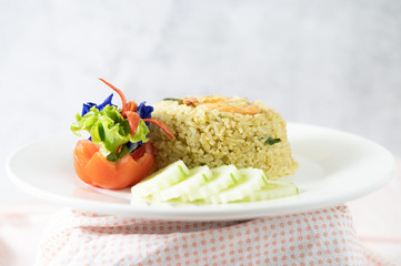 Shrimp fried rice on a white plate consisting of tomatoes and cucumbers.