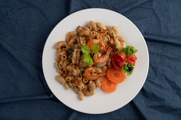 Stir shrimp macaroni on a white plate with carrots, tomatoes and salad.