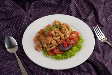 Stir shrimp macaroni on a white plate with fork, spoon, tomatoes and salad.