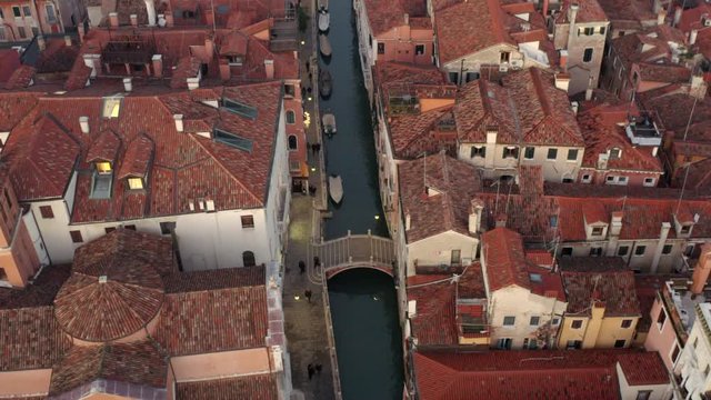 Aerial, drone shot tilting over people walking on a bridge, at a small channel, Venetian streets, on a evening, in Venice city, Italy