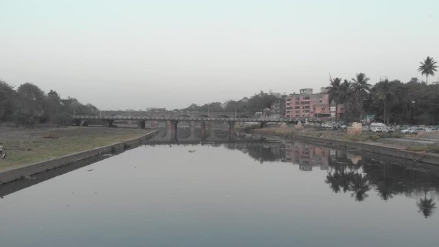 Drone shot over still river towards a busy bridge Pune India