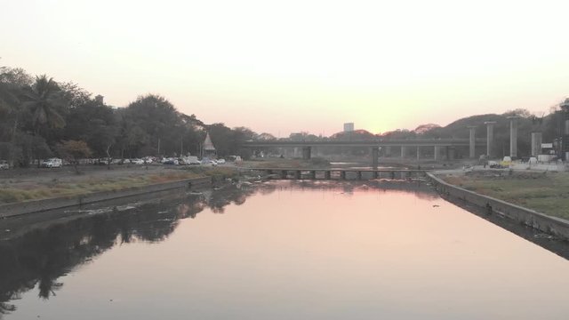 Drone shot over still river towards a bridge at sunset Pune